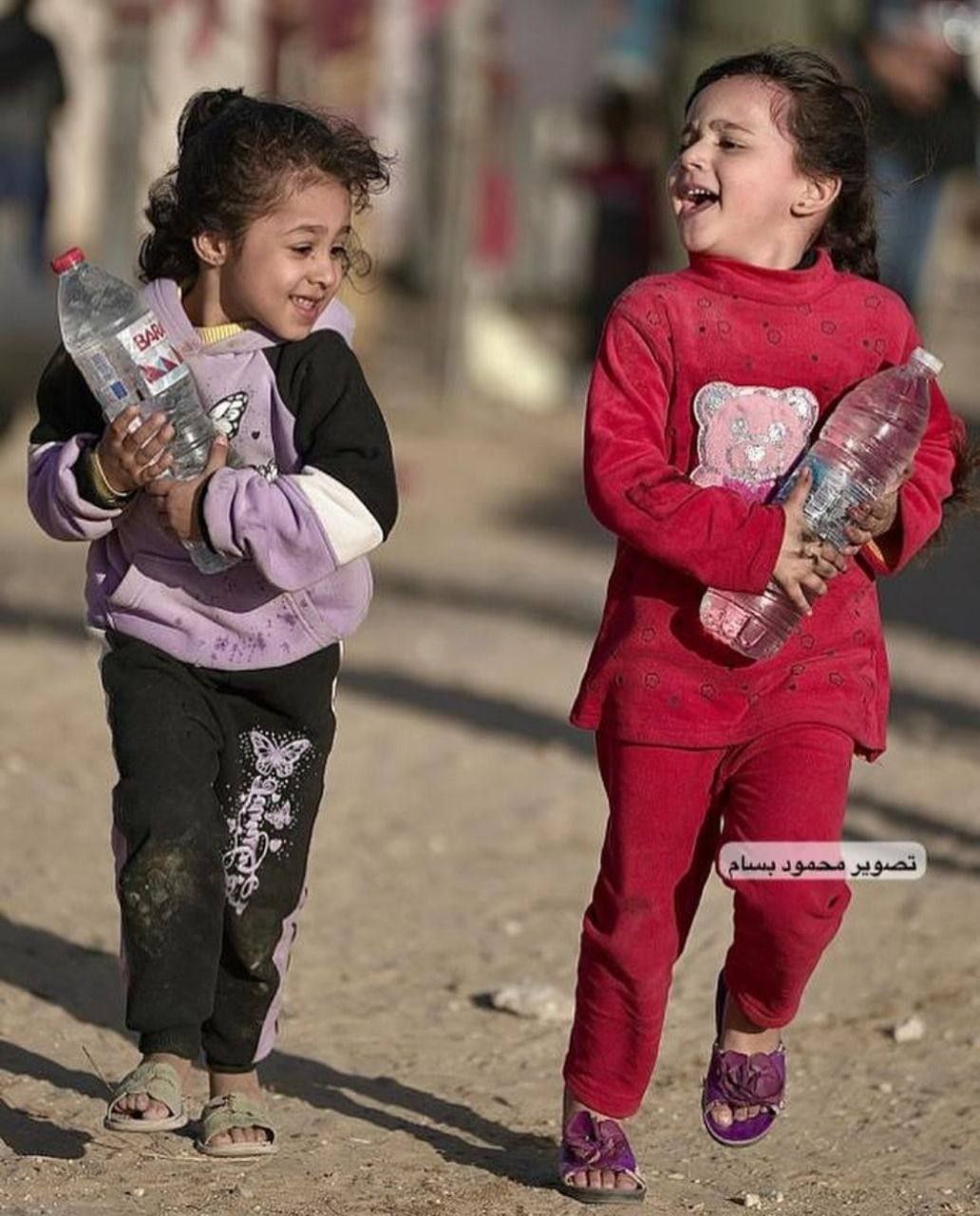 فرحة طفلتين نازحتين بعد حصولهن على قارورتي ماء لعوائلهن في ظل معاناة نقص المياه إثر الحصار الذي فرضه الاحتلال على غزة